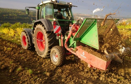 Ein grüner Traktor mit roten Rädern gräbt und hebt den Boden auf einem Feld mit Hilfe von landwirtschaftlichen Geräten, die an der Front angebracht sind. Erde und Pflanzenwurzeln fliegen in die Luft. Im Hintergrund sind üppige grüne Hügel zu sehen. Ein grüner Traktor mit roten Rädern gräbt und hebt den Boden auf einem Feld mit Hilfe von landwirtschaftlichen Geräten, die an der Front angebracht sind. Erde und Pflanzenwurzeln fliegen in die Luft. Im Hintergrund sind üppige grüne Hügel zu sehen.